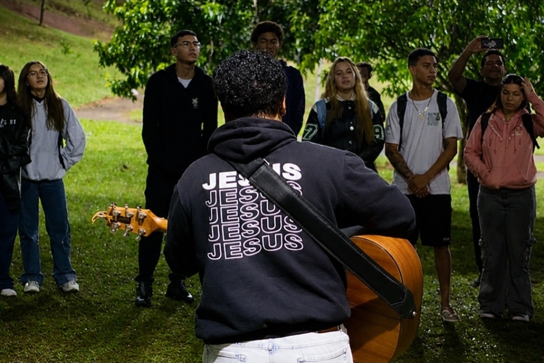 Jovem tocando violão para um grupo ao ar livre